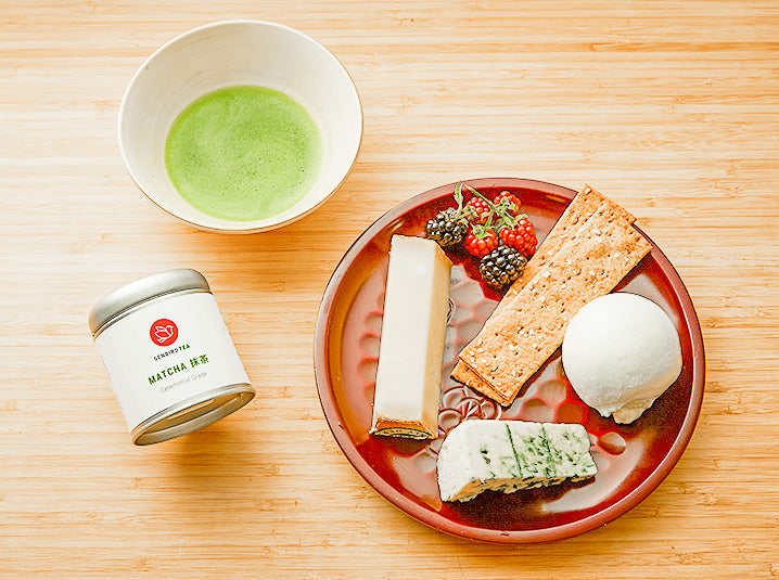 brewed green tea in a cup with tea tin and snacks in a plate