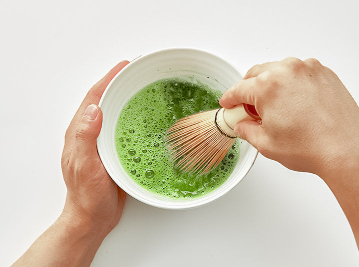 Hands whisking Match in a white ceramic bowl