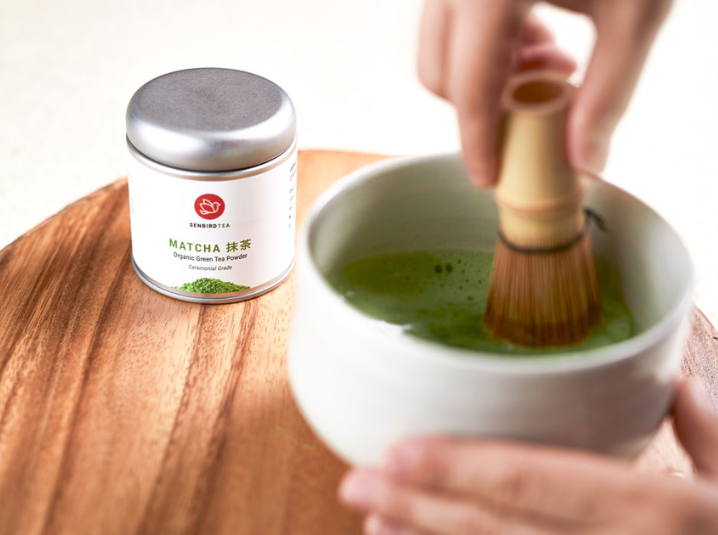 whisking matcha in a white bowl with match tea tin