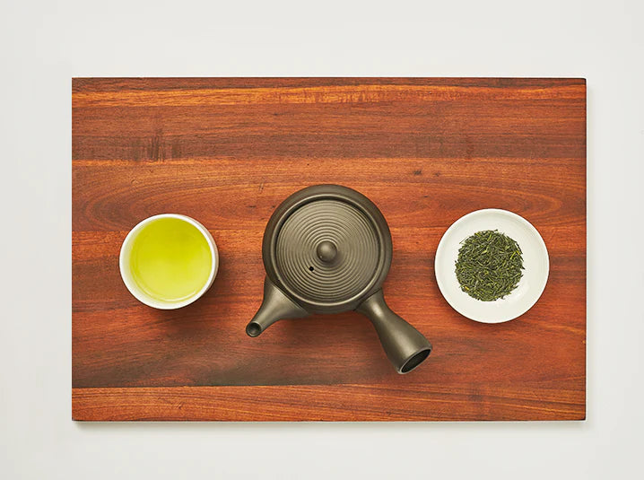 flat lay of shade-grown gyokuro green tea leaves beside a traditional Japanese kyusu teapot on a wooden surface