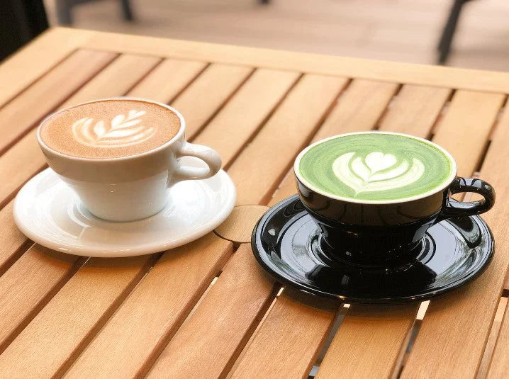 Hot matcha green tea latte and coffee latte side by side on a wooden table at a café with latte art
