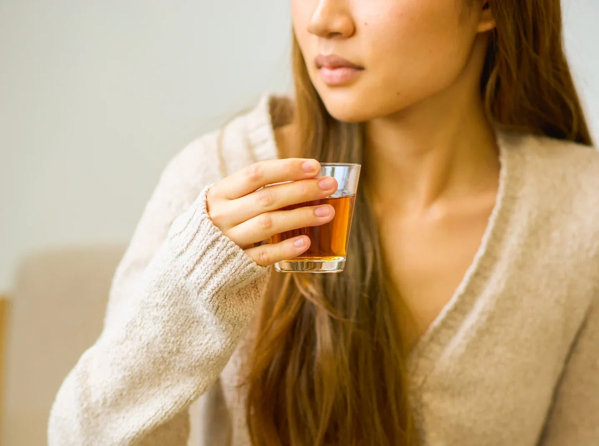 Person in a cream sweater holding a glass of amber Wakoucha Japanese black tea.