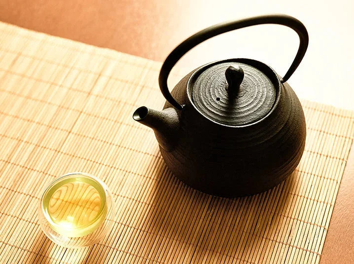 Japanese tetsubin cast iron teapot on bamboo mat with a glass cup of brewed green tea