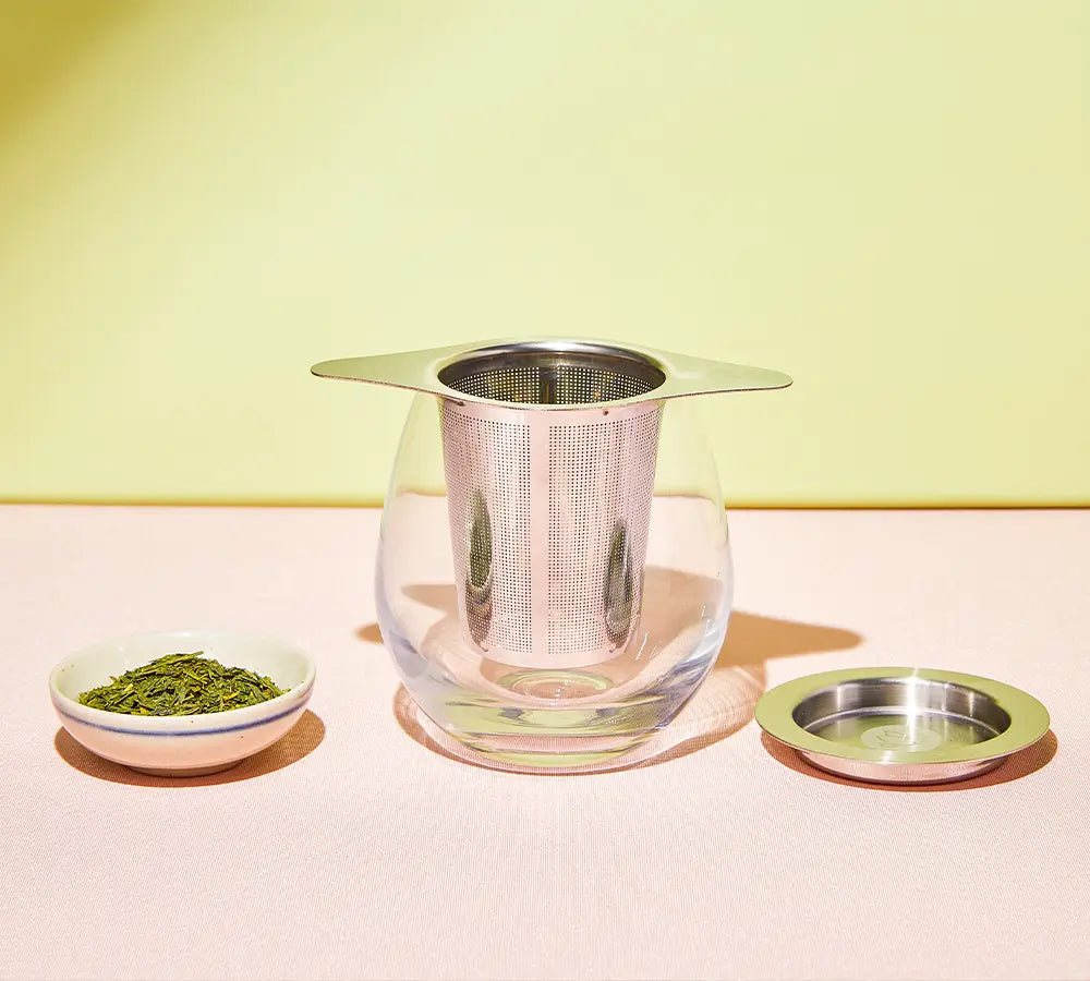 Japanese tea brewing with a stainless steel infuser in a glass cup and loose green tea leaves