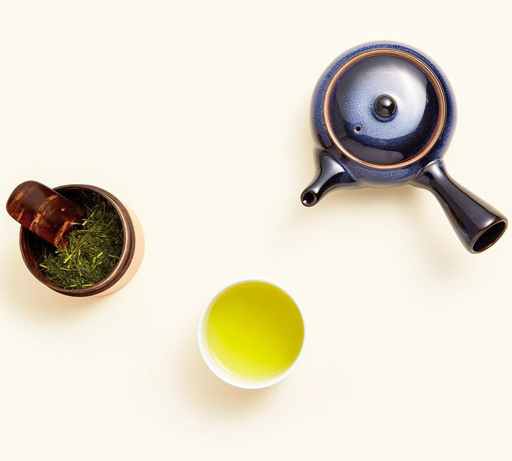 Overhead view of Japanese sencha tea with a blue kyusu teapot, teacup, and loose green tea leaves