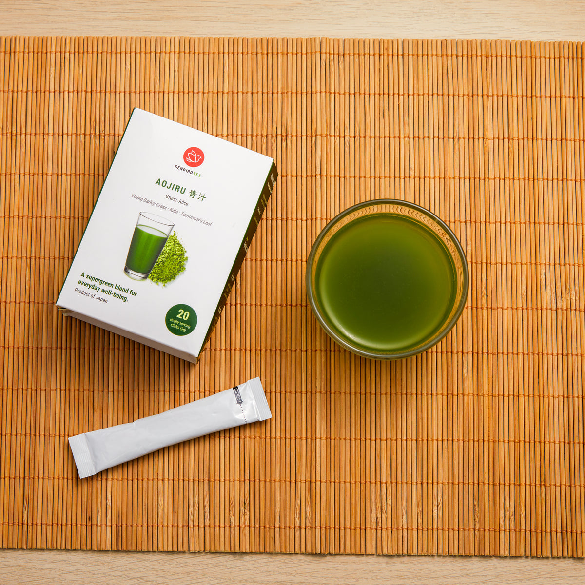 Overhead view of Senbird Aojiru Japanese green juice, its box and a single-serving stick on a bamboo mat