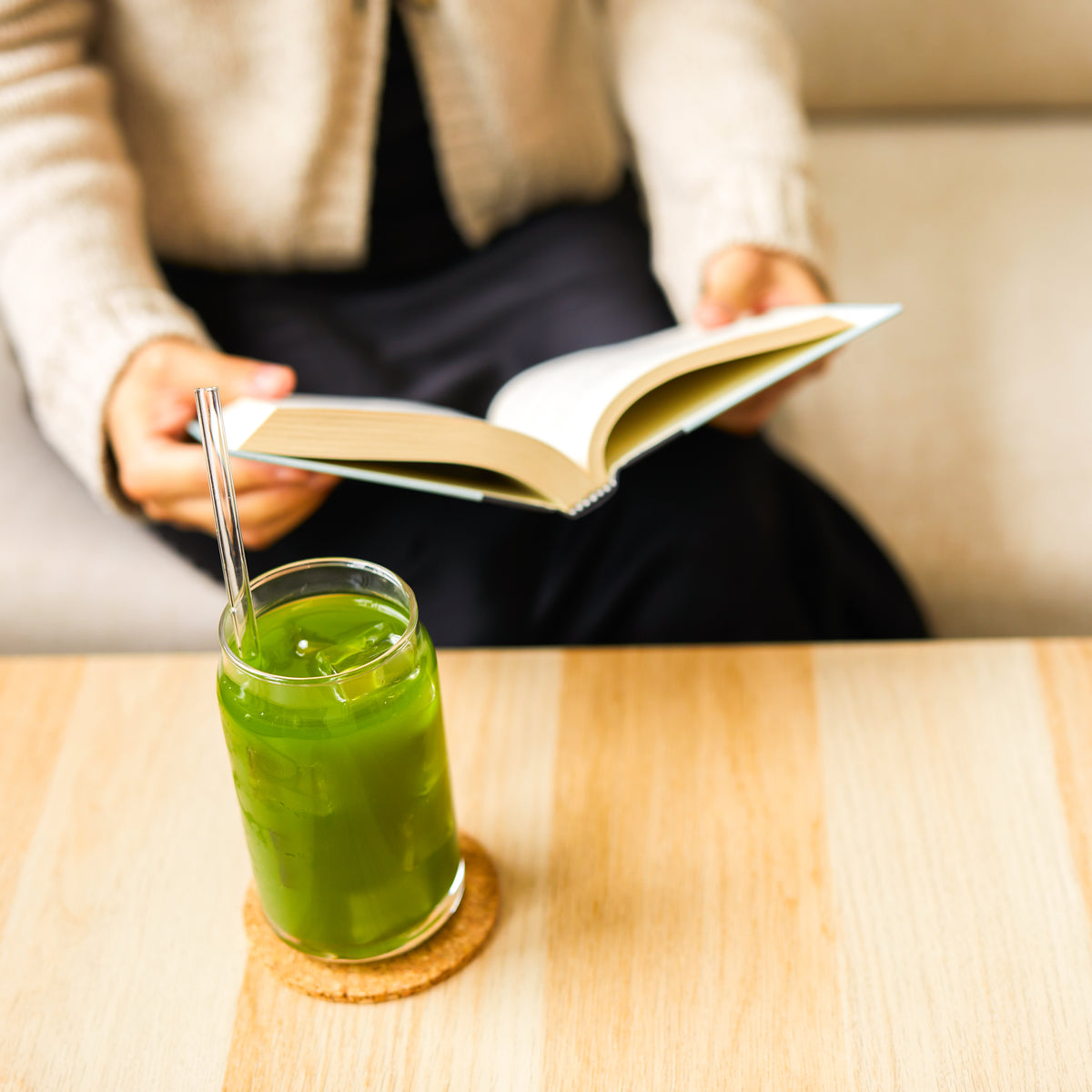 Iced Aojiru Japanese green juice on a wooden table beside a person reading an open book