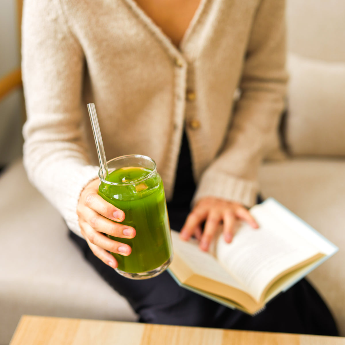 Person holding a glass of iced Aojiru Japanese green juice while reading a book at home