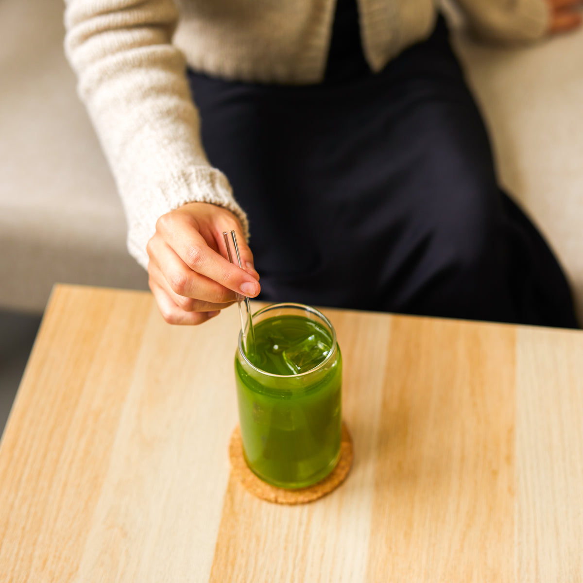 Hand stirring iced Aojiru Japanese green juice with a glass straw at a wooden table